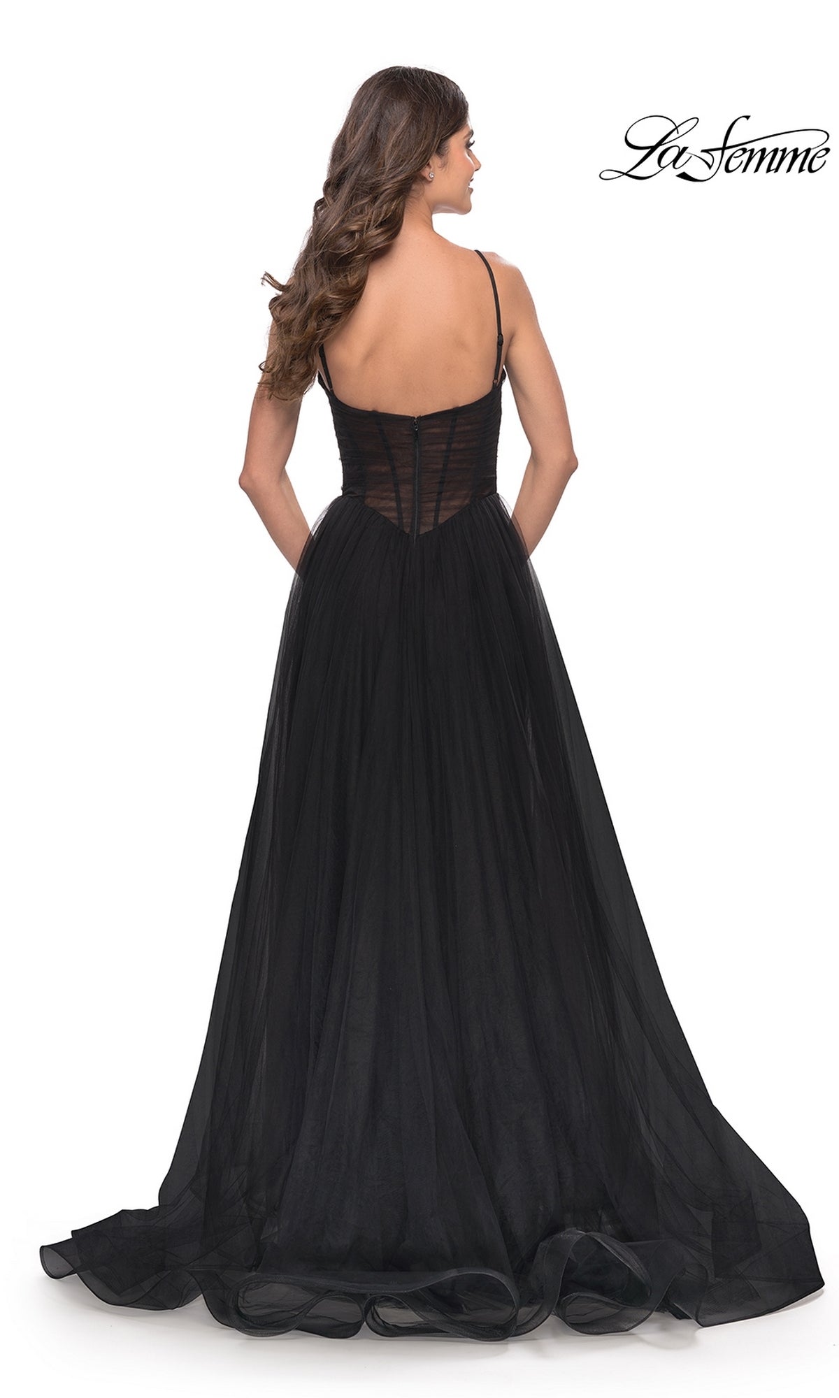 A woman faces away, showcasing the sheer back and flowing skirt of the Sheer-Waist La Femme Long Prom Ball Gown 31147, a black, floor-length dress with thin straps. The La Femme logo appears in the top right corner.